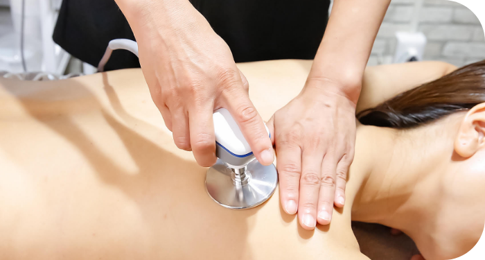 画像：ベッドに横になった女性に高周波温熱機器を使用して施術している