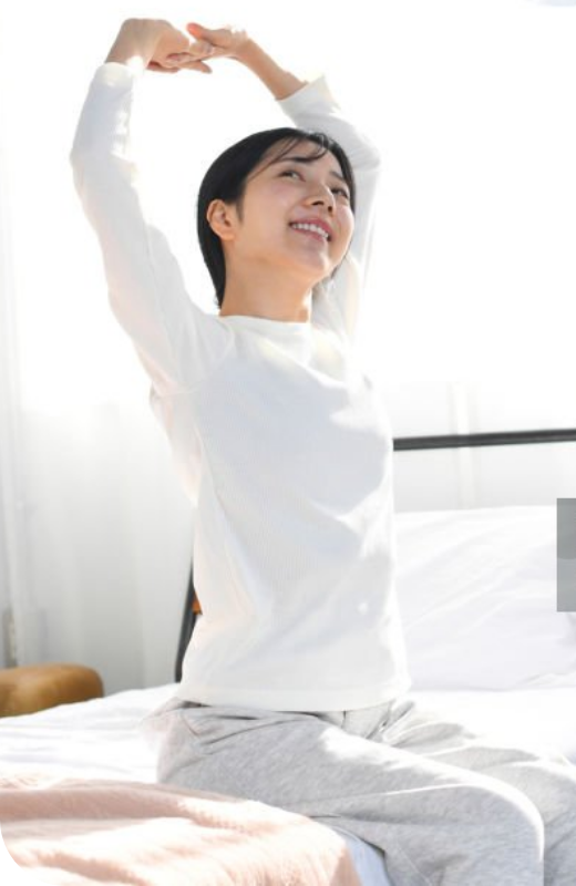 画像:女性がベッドの上で笑顔で腕を上げてストレッチをしている画像