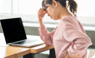 画像：PC前にいるピンク色の長袖姿の女性が、眉間と腰に手を当てている