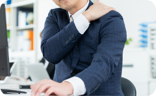 画像：紺色のスーツ姿の男性がPCの前で肩に手を当てている