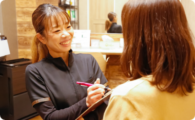 画像：紺色の制服を着た女性店員が、お客様の話を笑顔でヒアリングしている